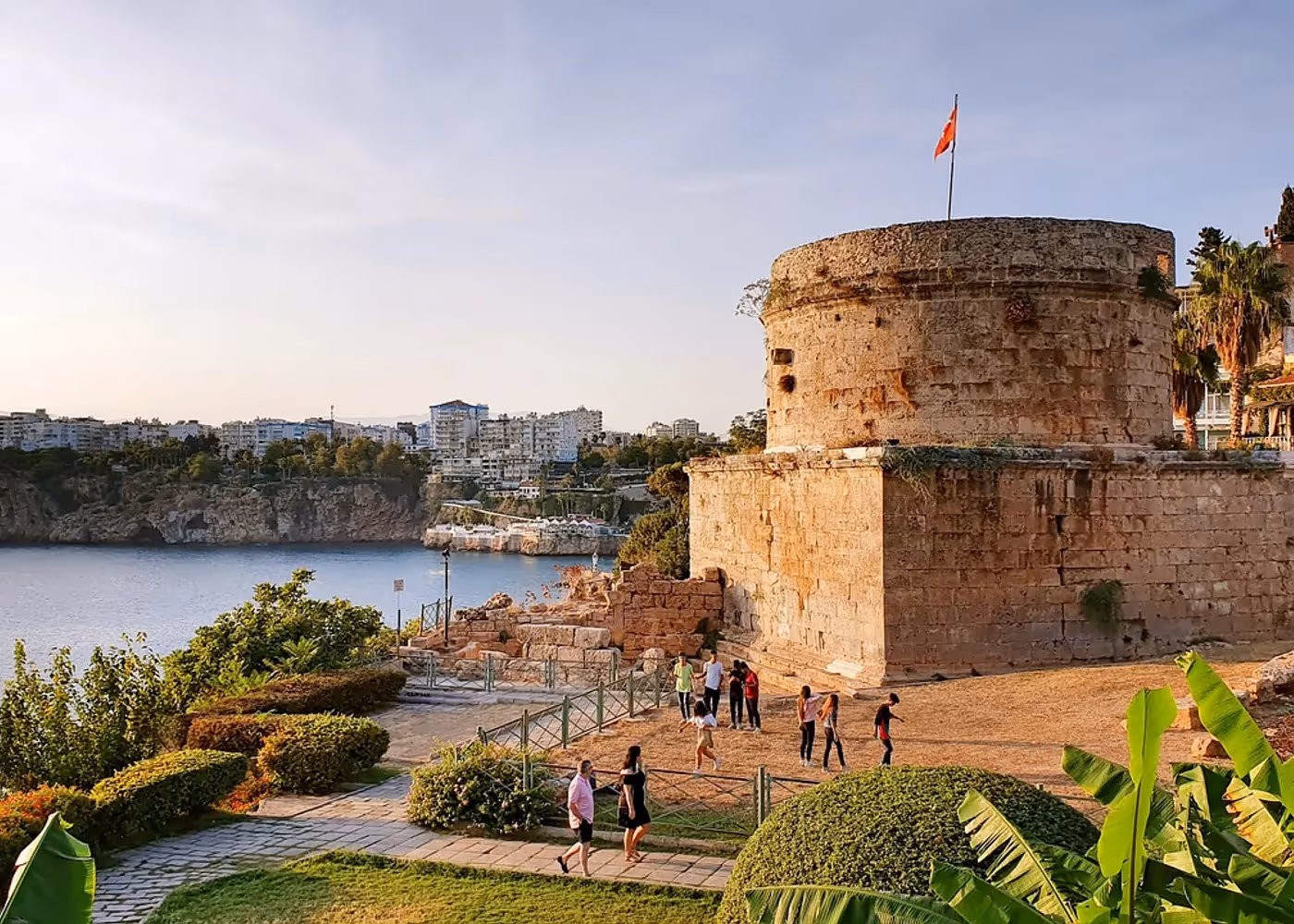 Grijze stenen toren tussen palmen en gras in het klifpark van Antalya