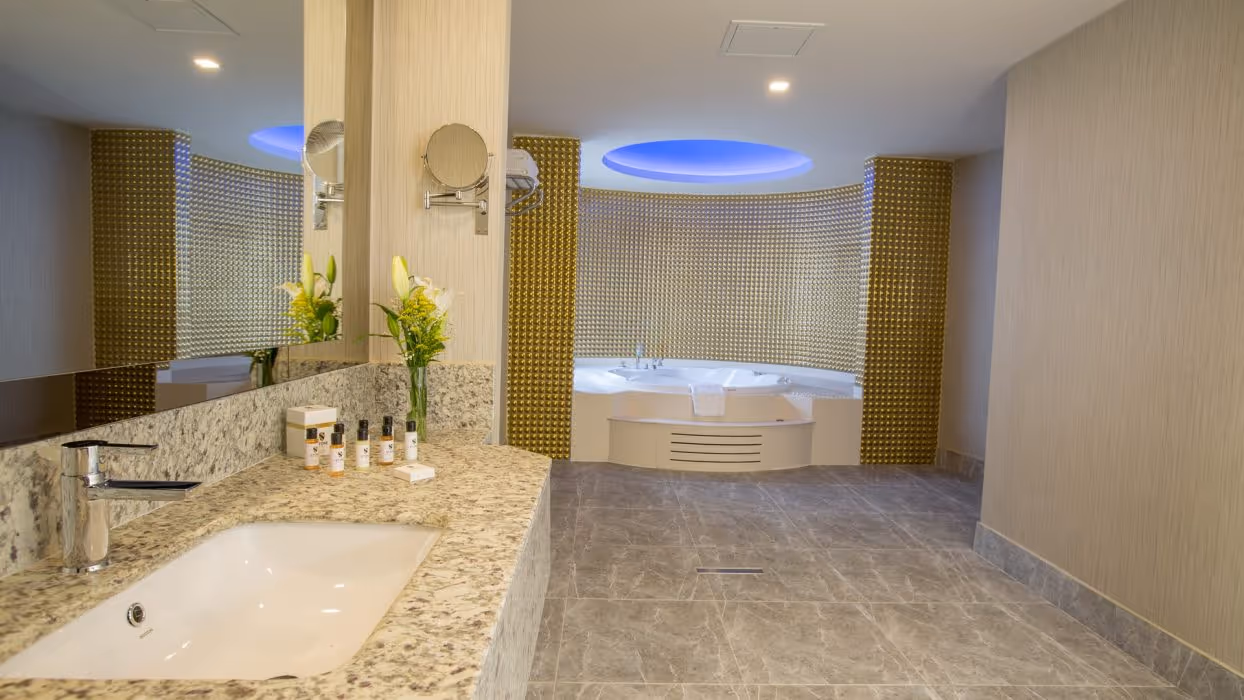 Badkamer van de deluxe suite met een rond bubbelbad onder een blauw verlicht plafond en een wastafel bij Royal Seginus in Lara