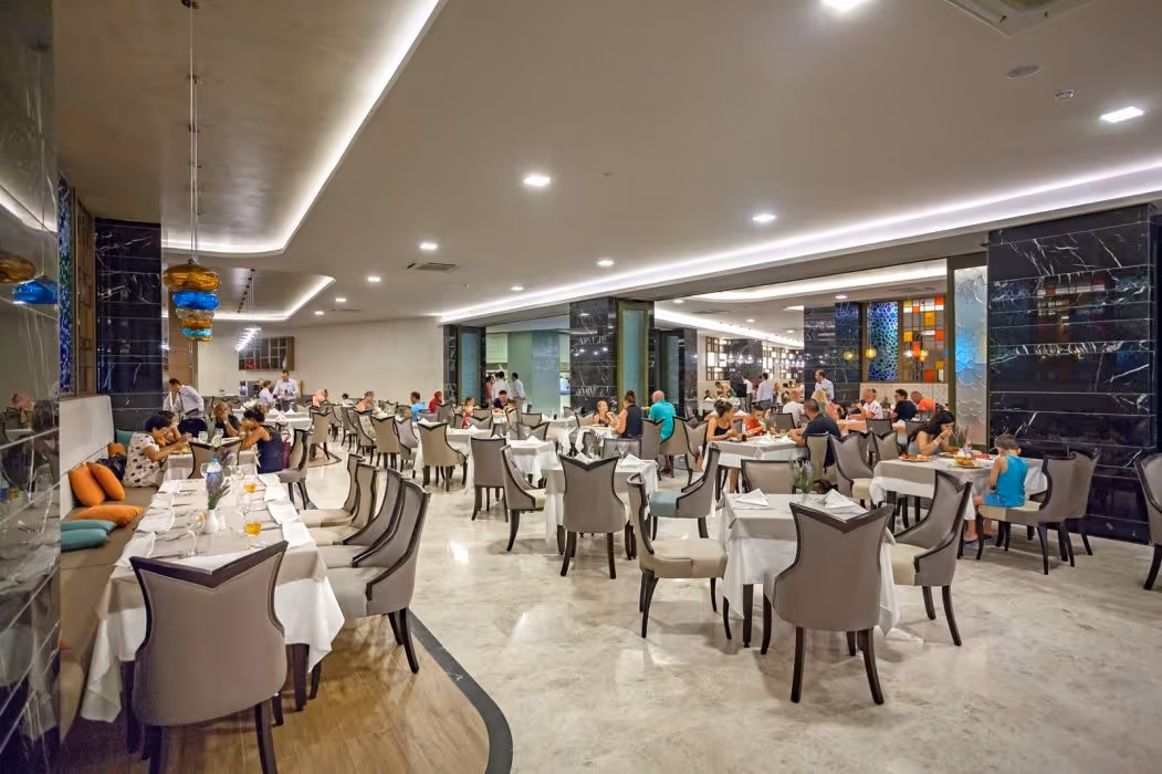 Restaurantzaal met gedekte tafels en gasten die eten onder een hoog plafond bij Royal Seginus in Lara