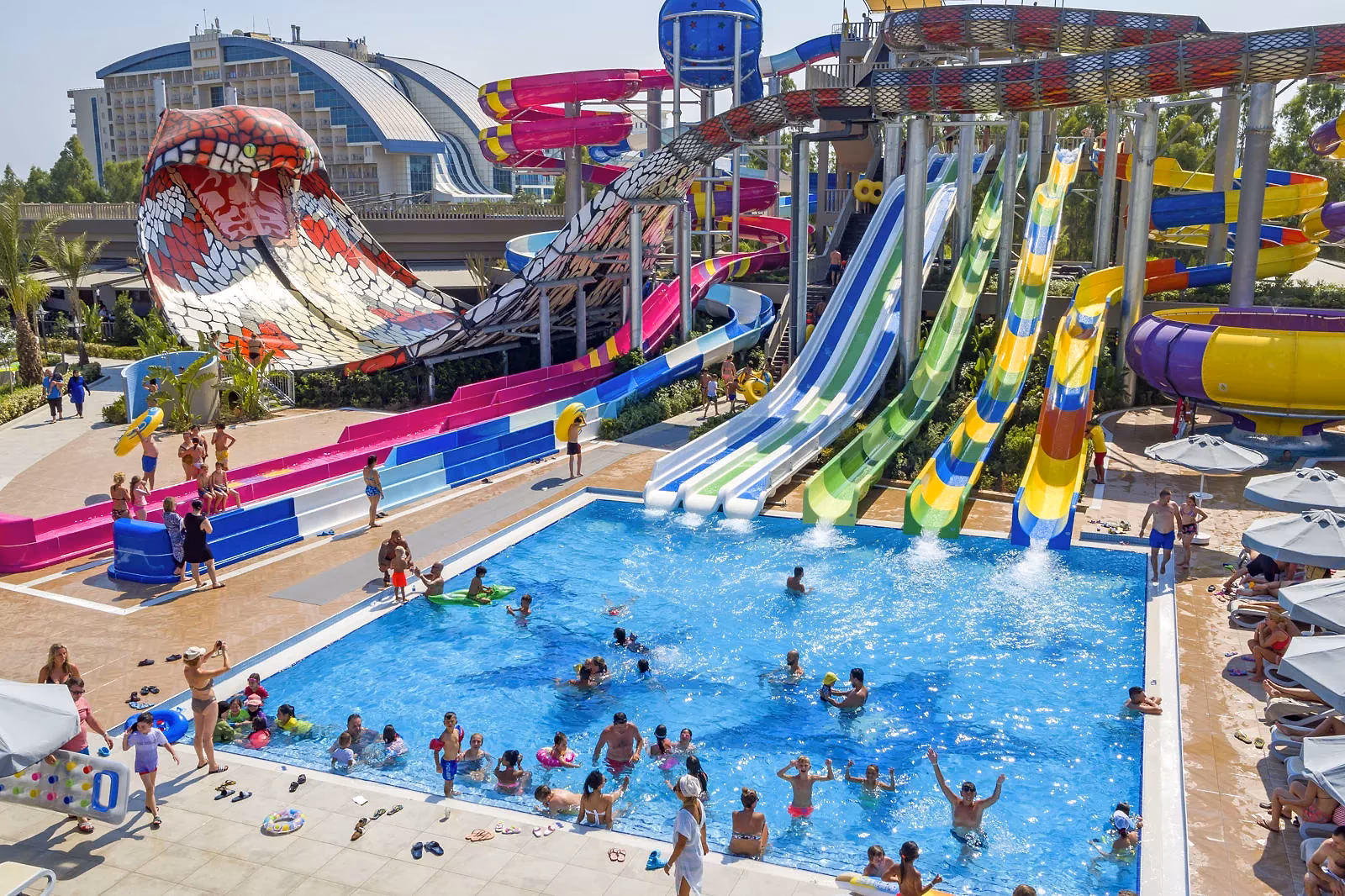 Glijbanen in rood, blauw, groen en geel boven een zwembad met zwemmende gasten bij het aquapark van Royal Seginus in Lara