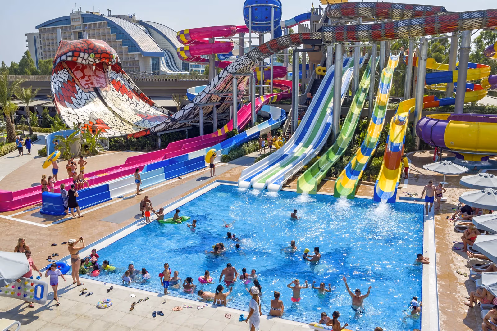 Glijbanen in rood, blauw, groen en geel boven een zwembad met zwemmende gasten bij het aquapark van Royal Seginus in Lara