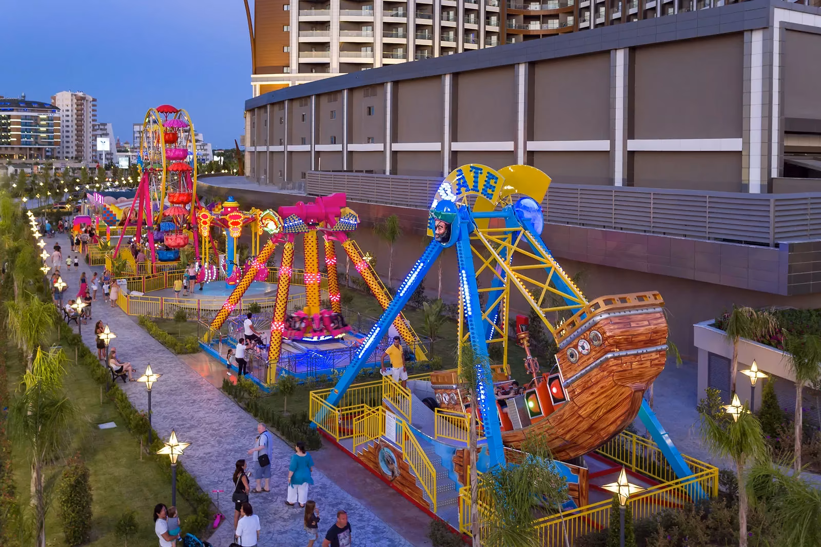 Kermisattracties in de vorm van een piratenschip en een draaimolen, 's avonds verlicht, in het lunapark van Royal Seginus in Lara