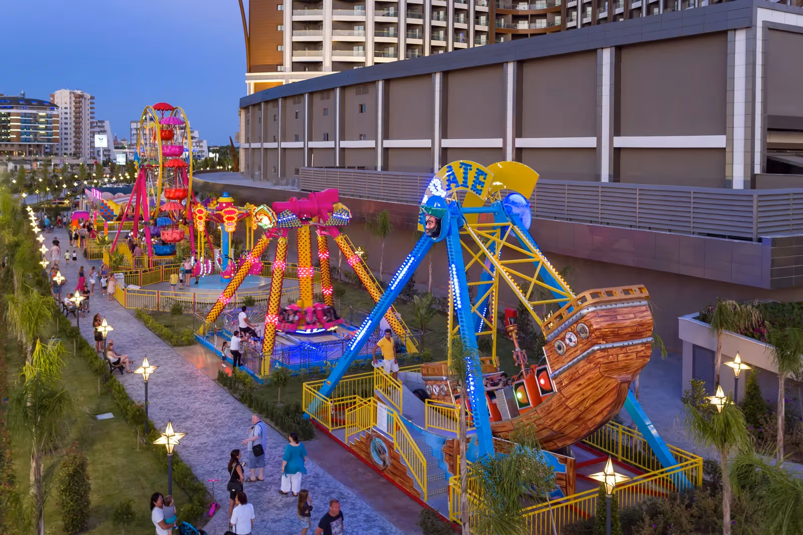 Kermisattracties in de vorm van een piratenschip en een draaimolen, 's avonds verlicht, in het lunapark van Royal Seginus in Lara