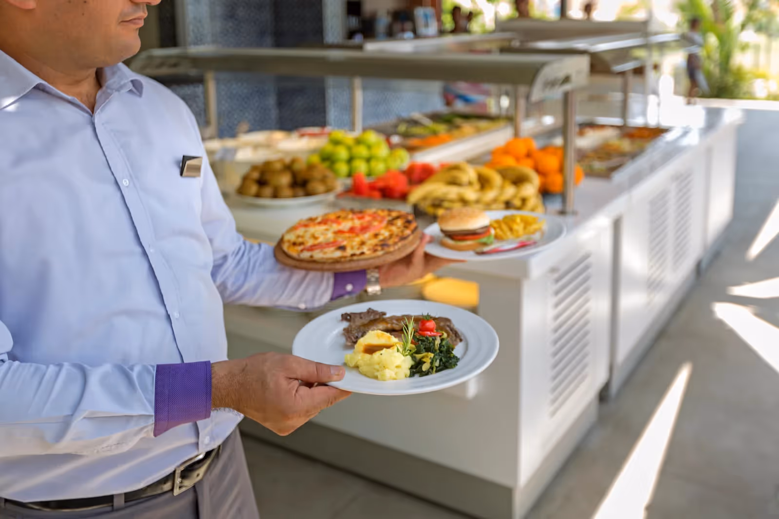 Een ober houdt een bord met pizza, vlees en groenten voor een buffet met vers fruit bij Royal Seginus in Lara