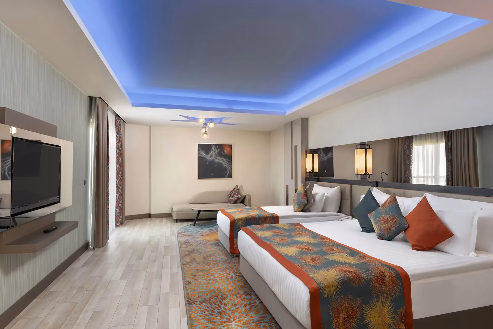Slaapgedeelte van de junior suite met bedden, een tv en een zithoek onder een blauw verlicht plafond bij Royal Seginus in Lara