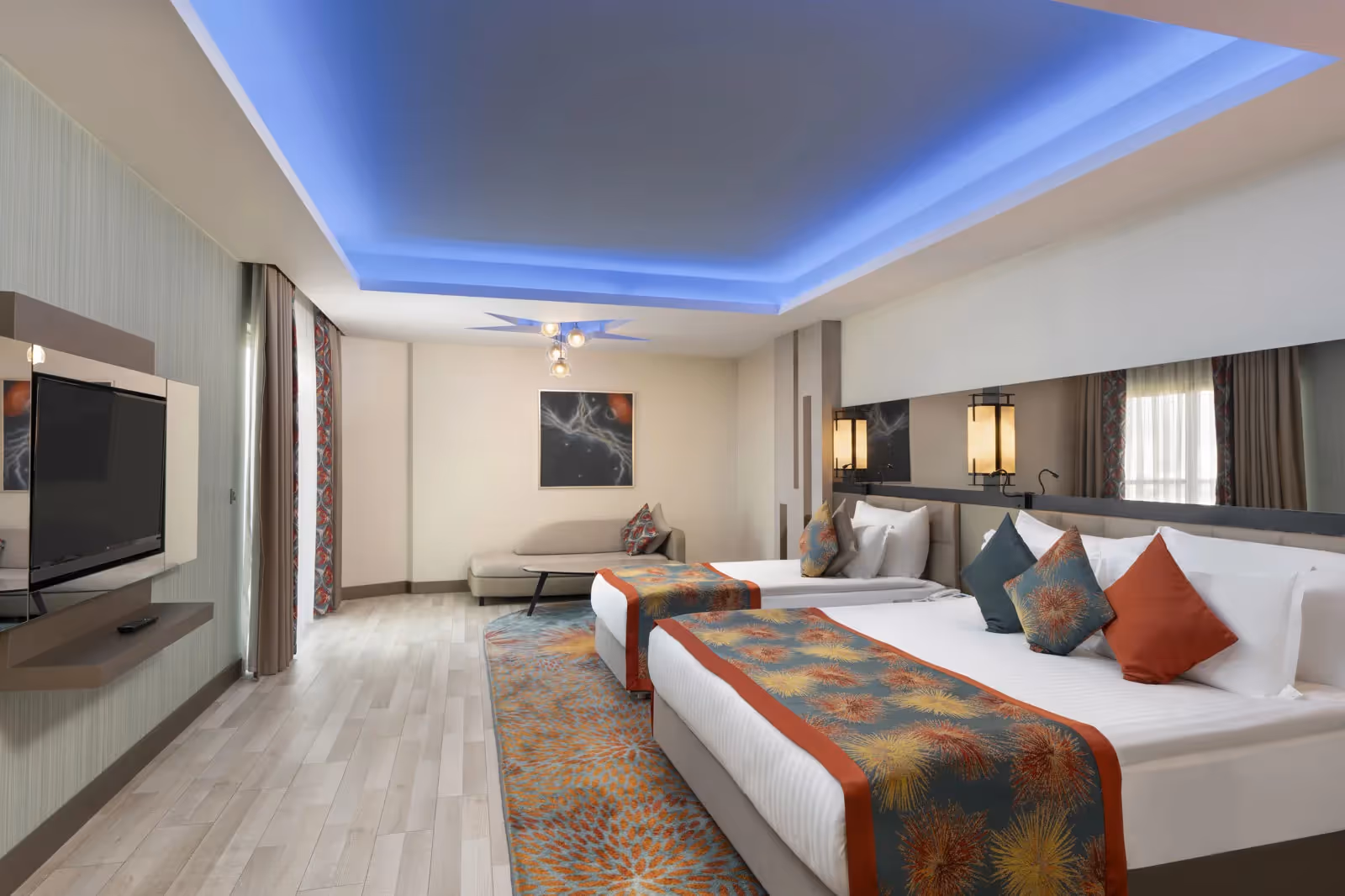 Slaapgedeelte van de junior suite met bedden, een tv en een zithoek onder een blauw verlicht plafond bij Royal Seginus in Lara