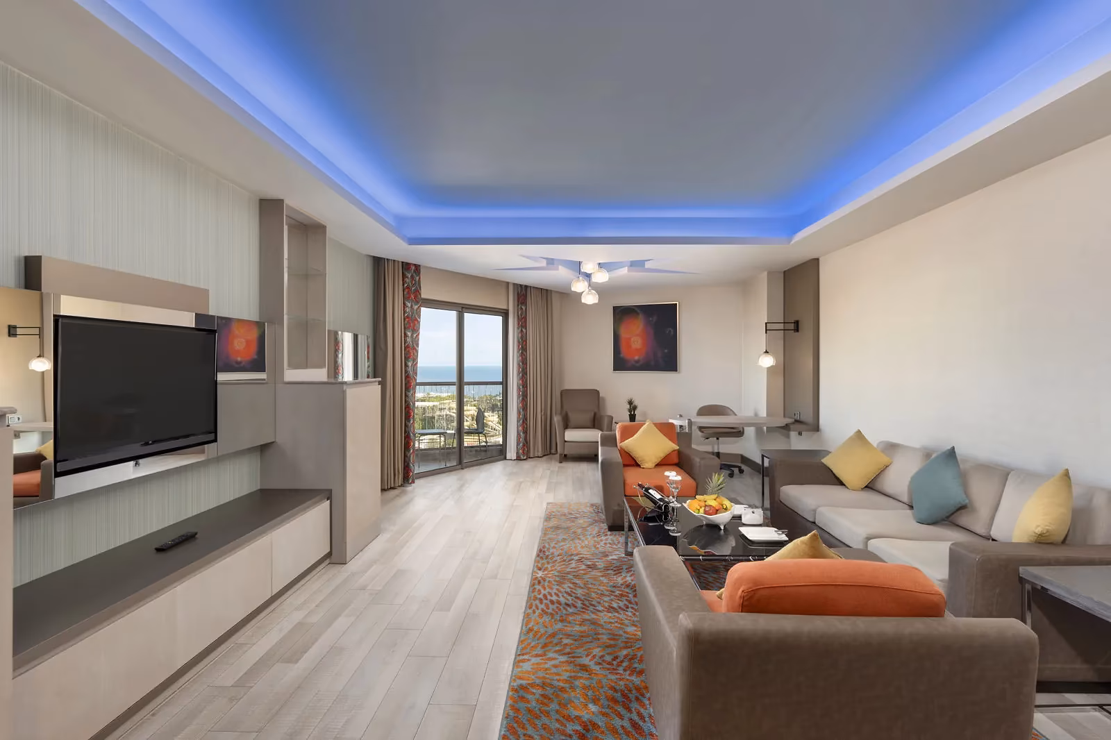 Woongedeelte van de junior suite met een hoekbank, een tv-wand en balkondeuren bij Royal Seginus in Lara