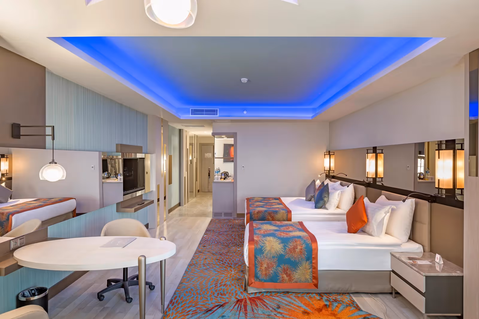 Tweepersoonskamer met bedden, een ronde tafel met bureaustoel en een blauw verlicht plafond bij Royal Seginus in Lara