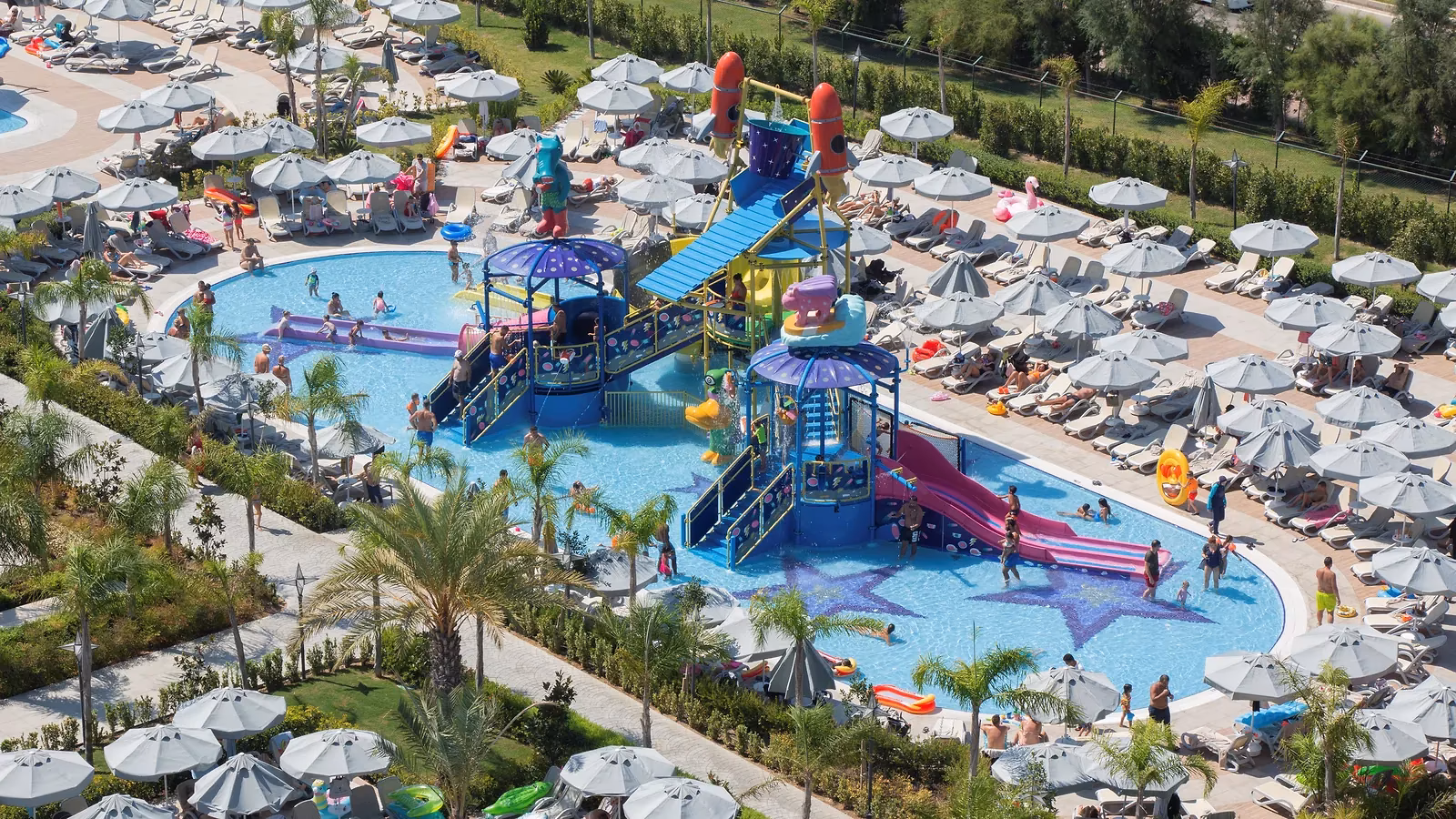 Luchtfoto van de waterspeeltuin met glijbaantjes in het kinderbad, omringd door ligbedden en parasols bij Royal Seginus in Lara