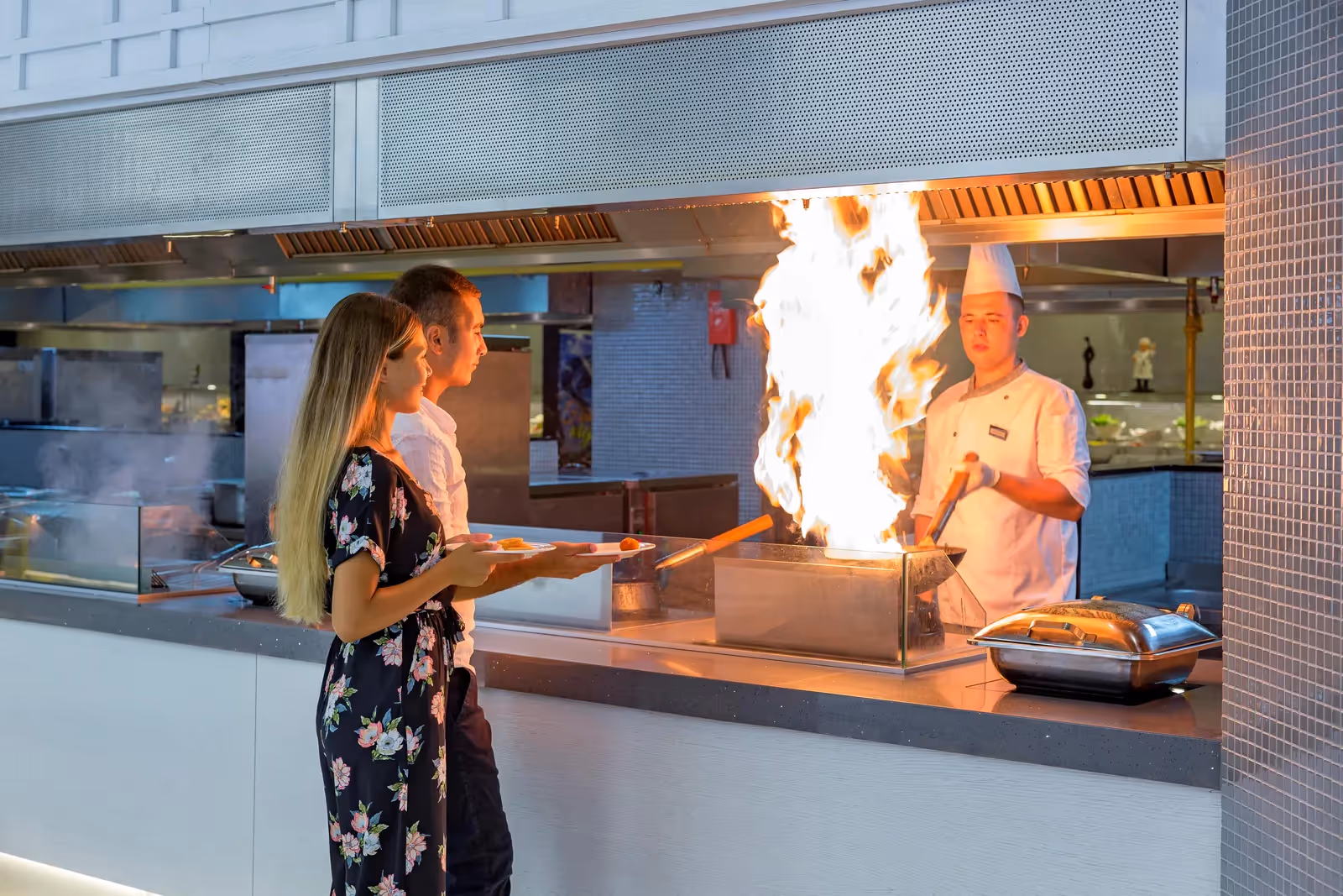Een kok bereidt een gerecht met vlammen aan het live-cookingstation terwijl twee gasten toekijken bij Royal Seginus in Lara