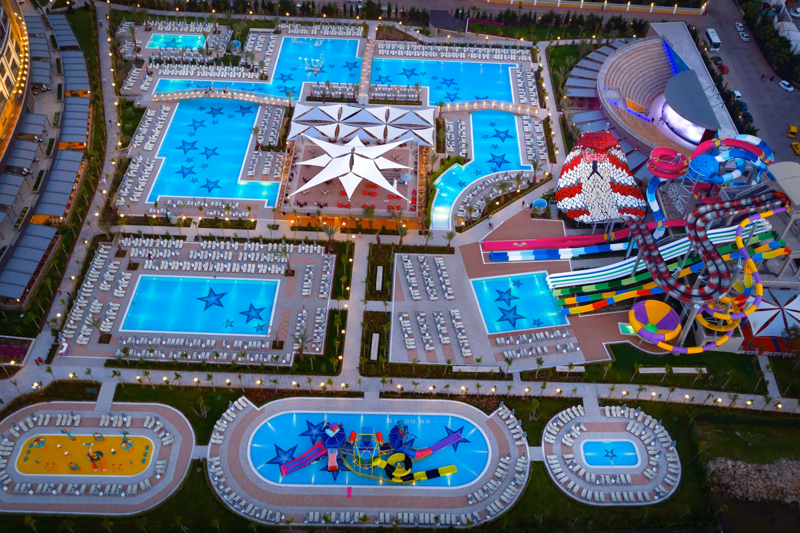 Luchtfoto van het zwembadlandschap met een stervormig plein, baden en het aquapark met kleurrijke glijbanen bij Royal Seginus in Lara