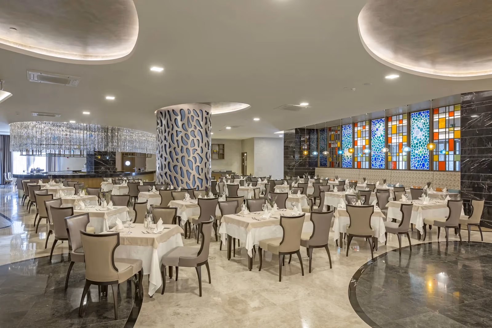 Restaurantzaal met gedekte tafels, een marmeren vloer en kleurrijke glas-in-loodramen bij Royal Seginus in Lara