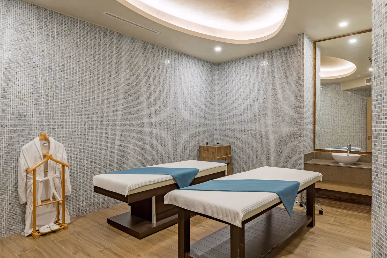 Massageruimte met twee behandeltafels, badjassen en een mozaïekwand bij Royal Seginus in Lara