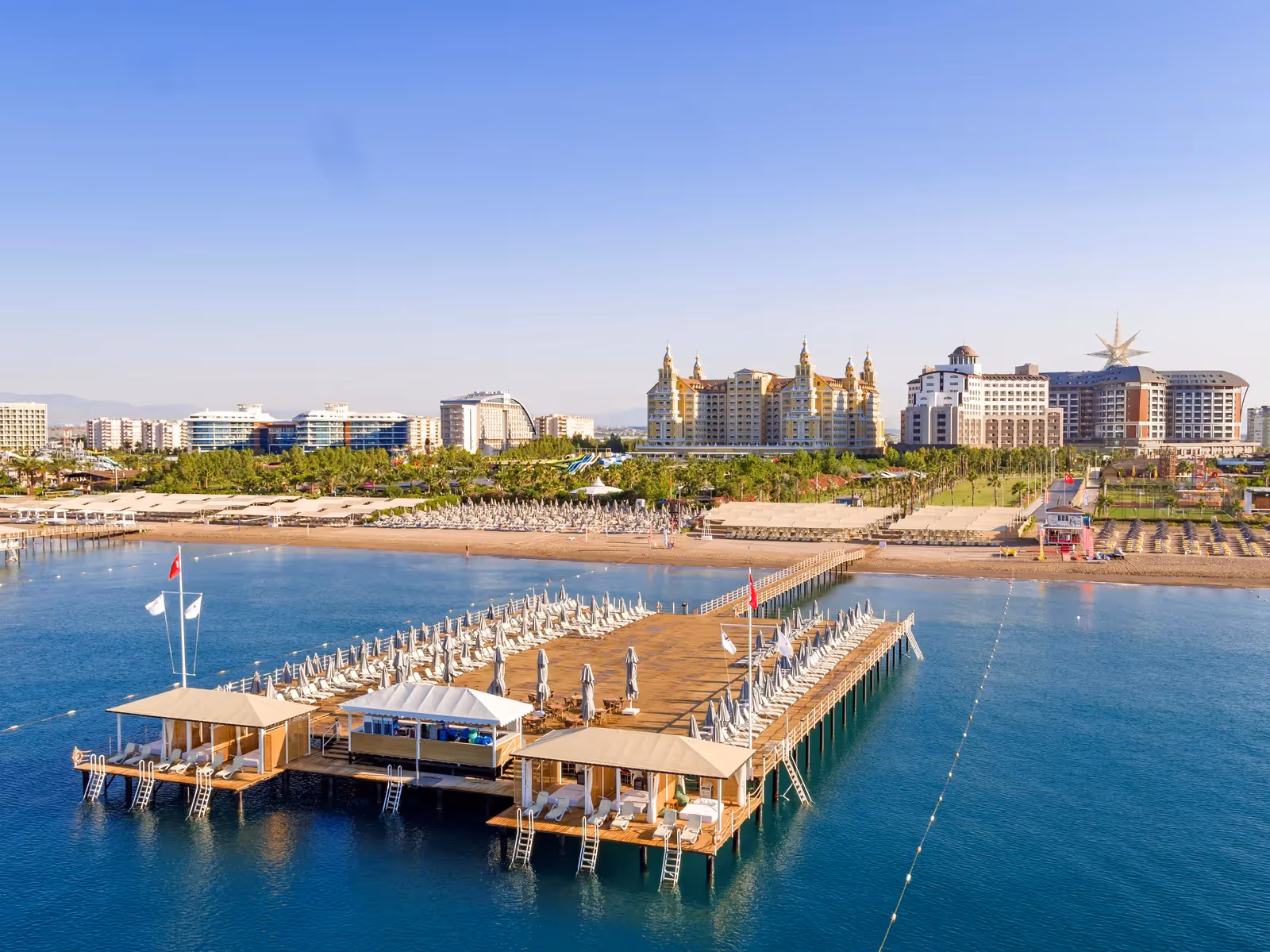 Luchtfoto van de houten pier met ligbedden in de zee, met hotels langs de kust bij Royal Seginus in Lara