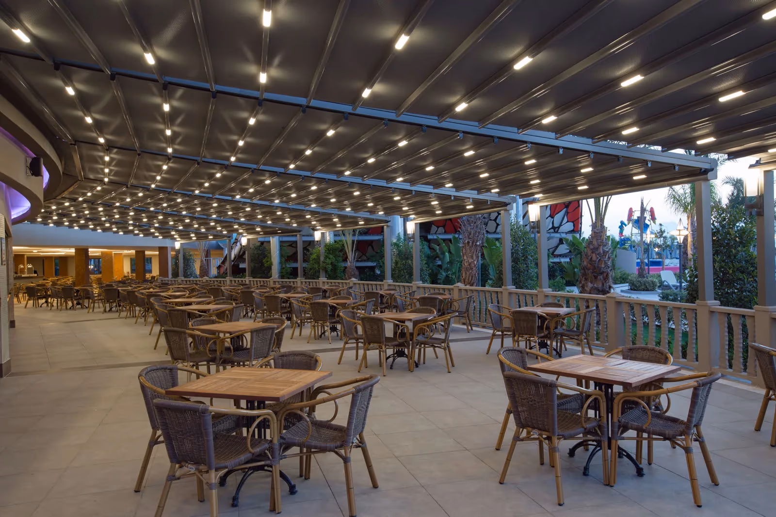 Overdekt terras met tafels en rieten stoelen, 's avonds verlicht, bij Royal Seginus in Lara