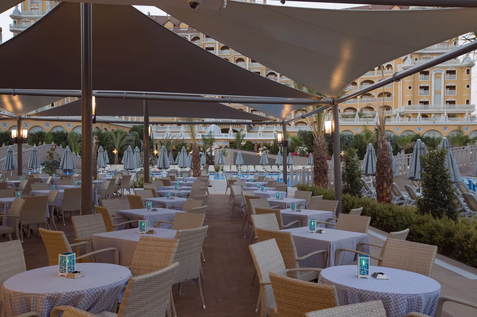 Terras met ronde tafels onder zonnezeilen naast de zwembaden bij Royal Seginus in Lara